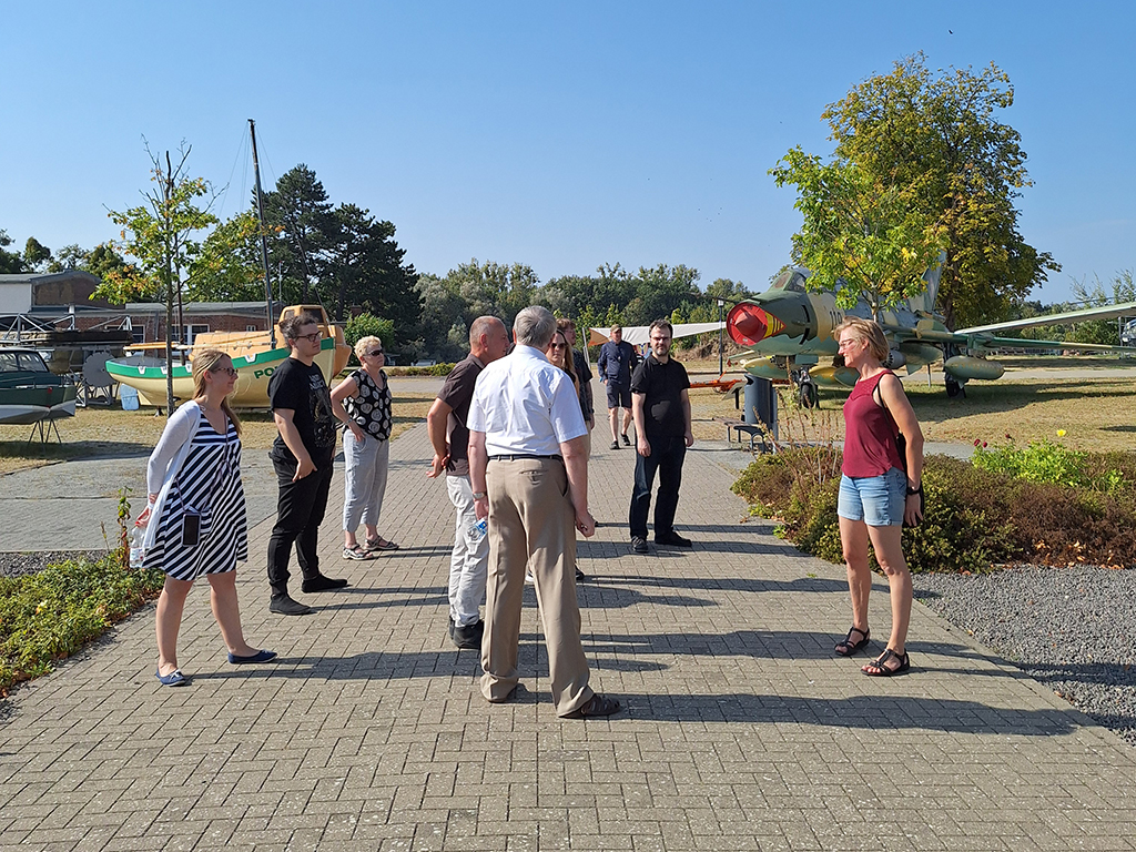 Teammitglieder erkunden gemeinsam ein Outdoor-Museum mit historischen Ausstellungsstücken. Die Gruppe ist in einer interessanten Unterhaltung vertieft.